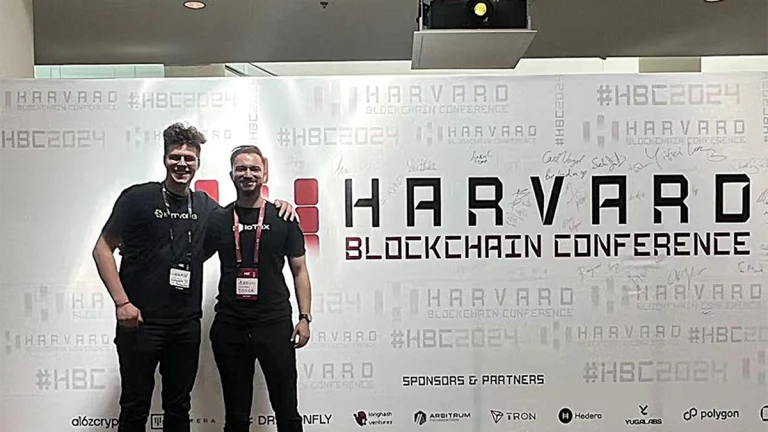 Two speakers at the Harvard Blockchain Conference 2025 posing in front of the official event banner